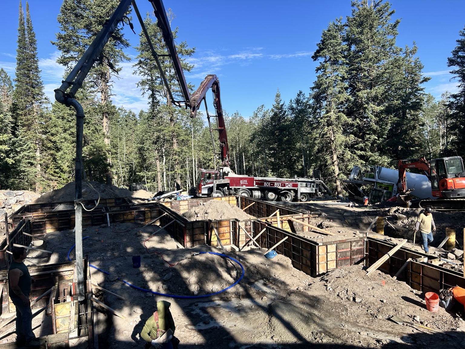 Envision boom pump placing a foundation at a wooded Utah mountain jobsite